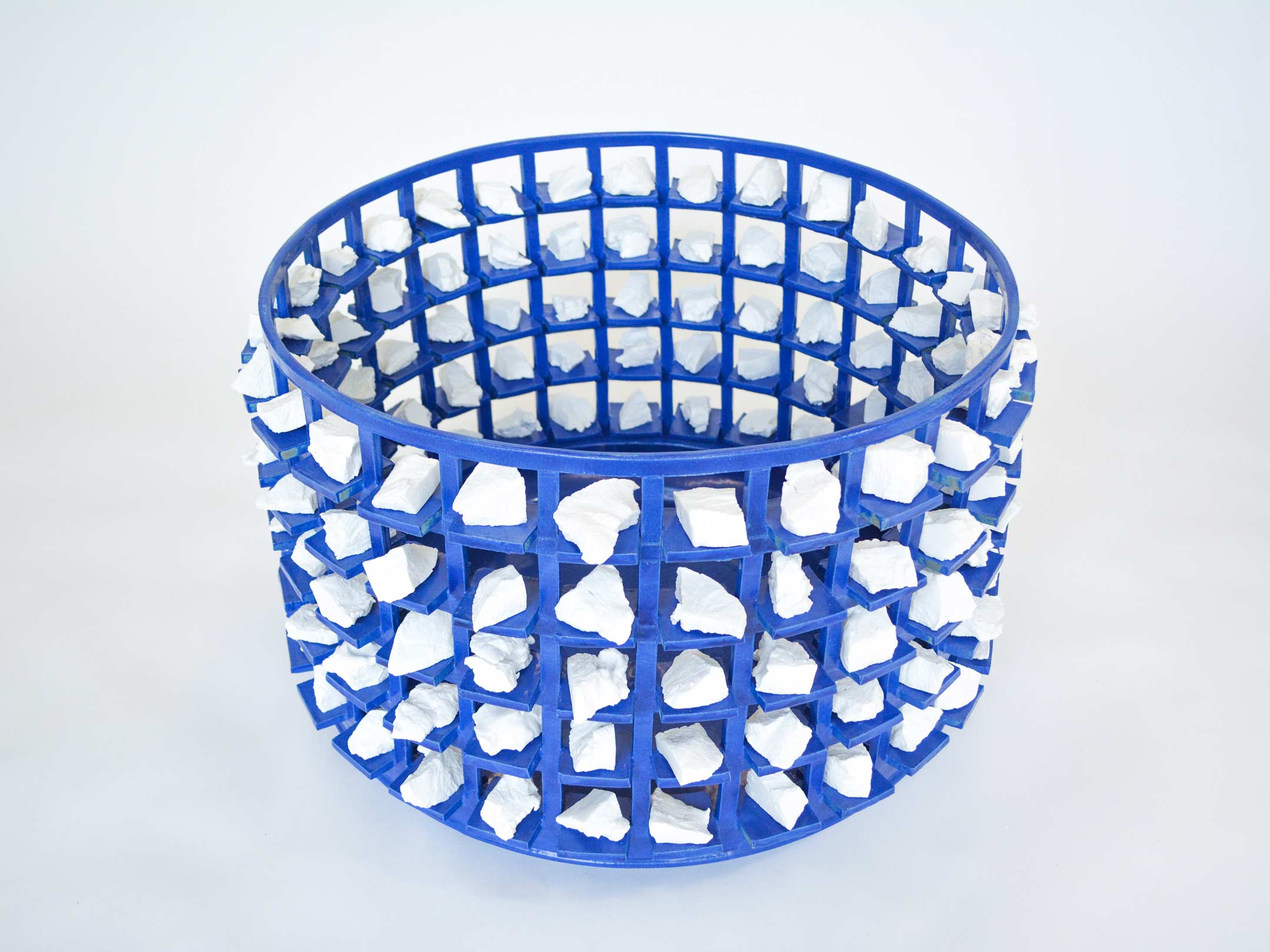 Large, wide blue stoneware vessel. Exterior is made up of a grid structure. Irregular white stones are inserted into the spaces formed by the grid.